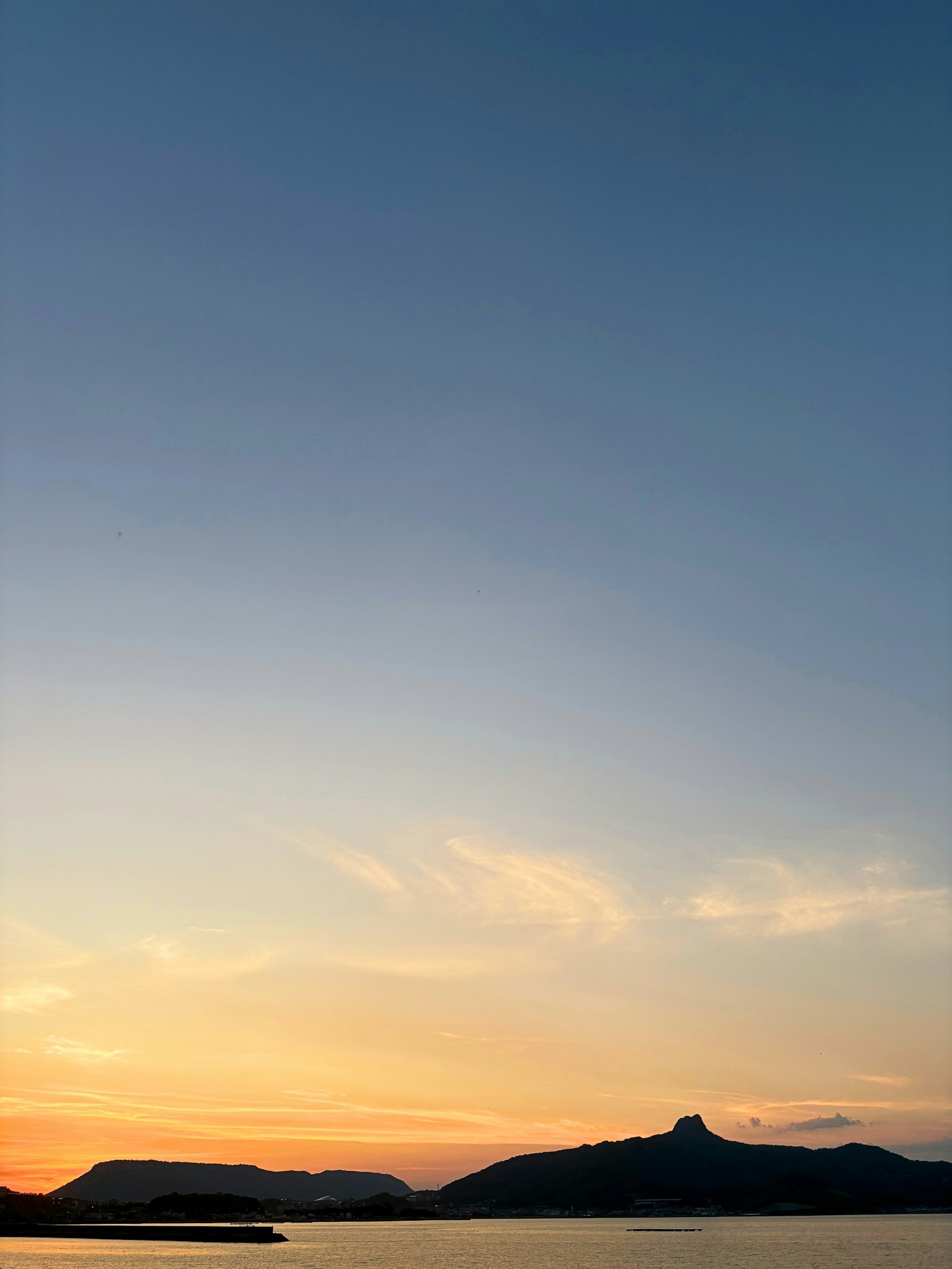Sonnenuntergang über dem Meer mit Bergen im Hintergrund blauer Himmel und orangefarbene Wolken