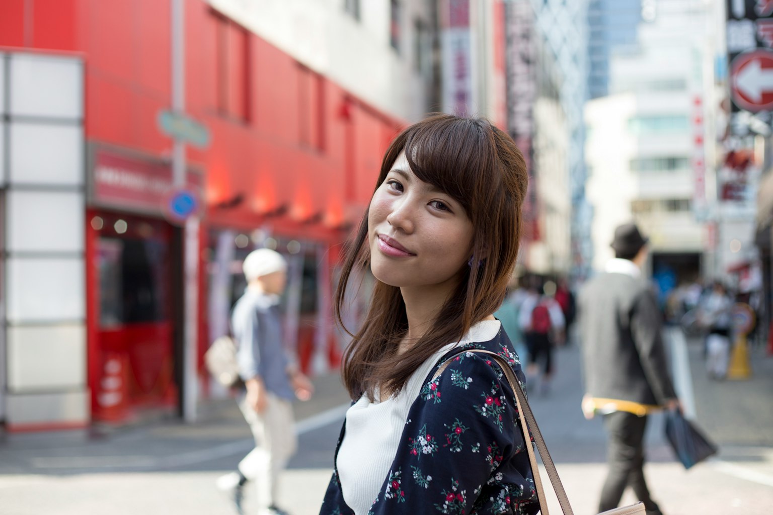 Portrait of a smiling woman in a city street with red buildings and pedestrians in the background