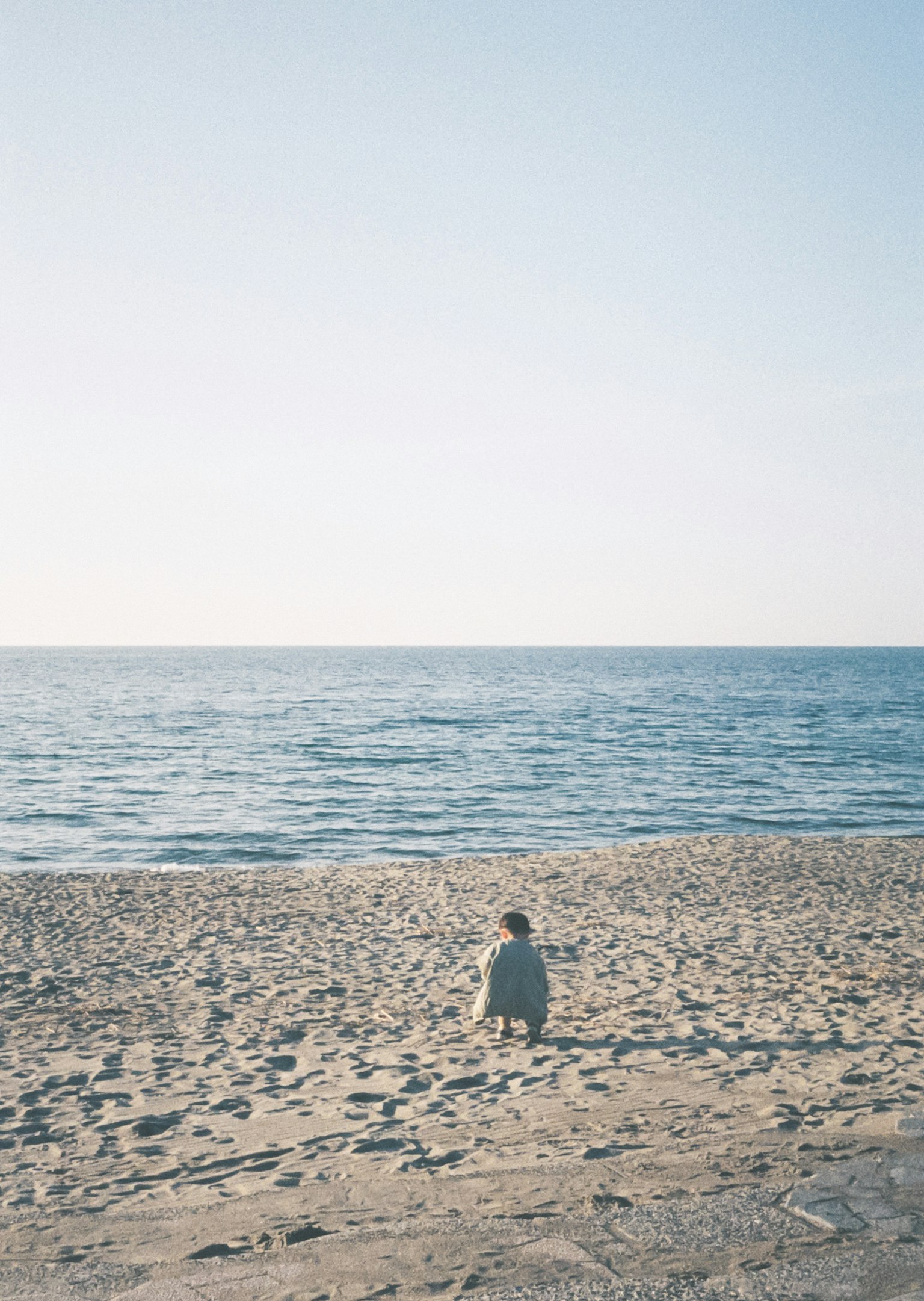 Person sitzt am Strand und schaut auf das Meer
