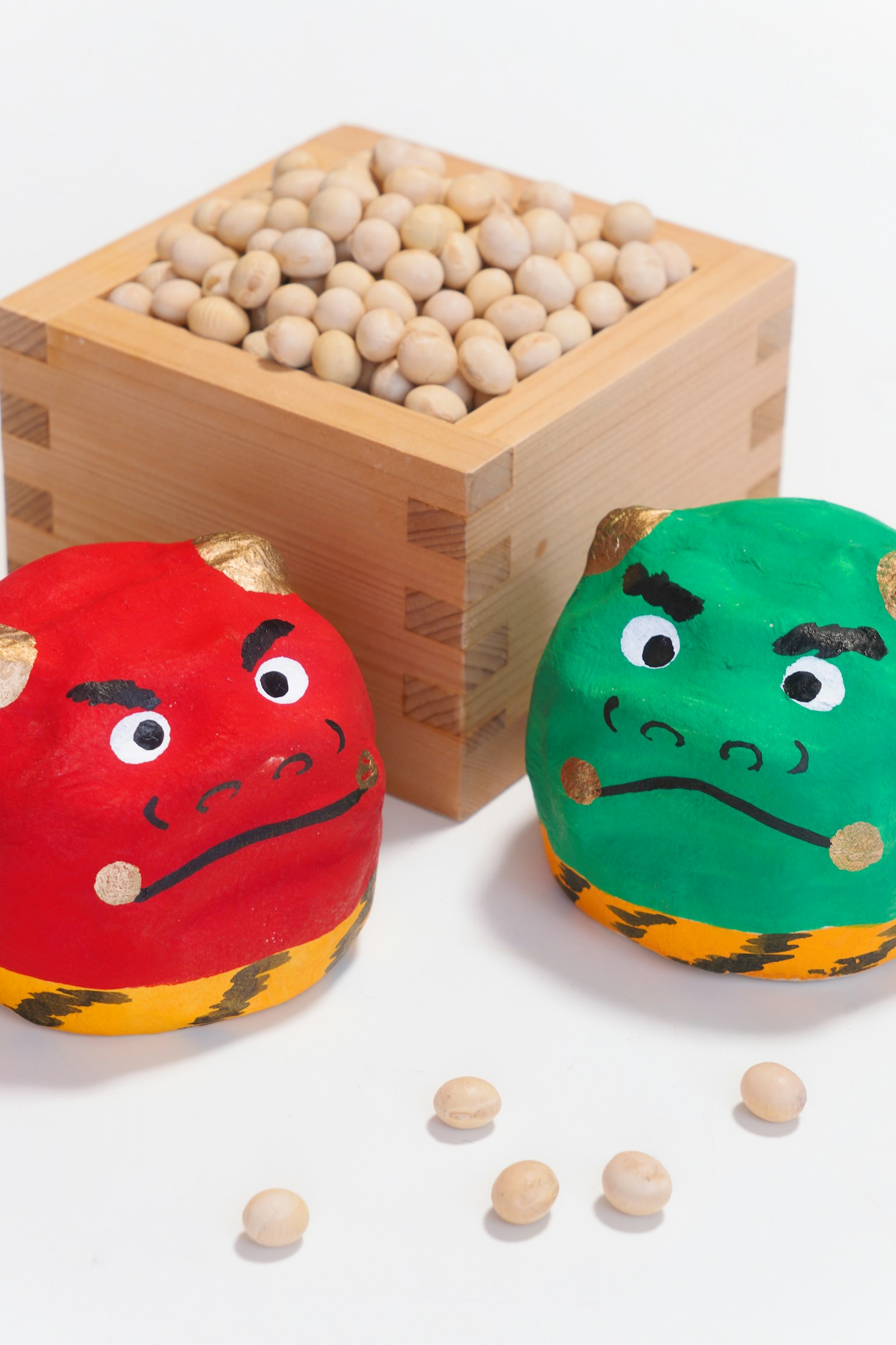 Personajes de demonios rojos y verdes en juguetes redondos con una caja de madera llena de soja