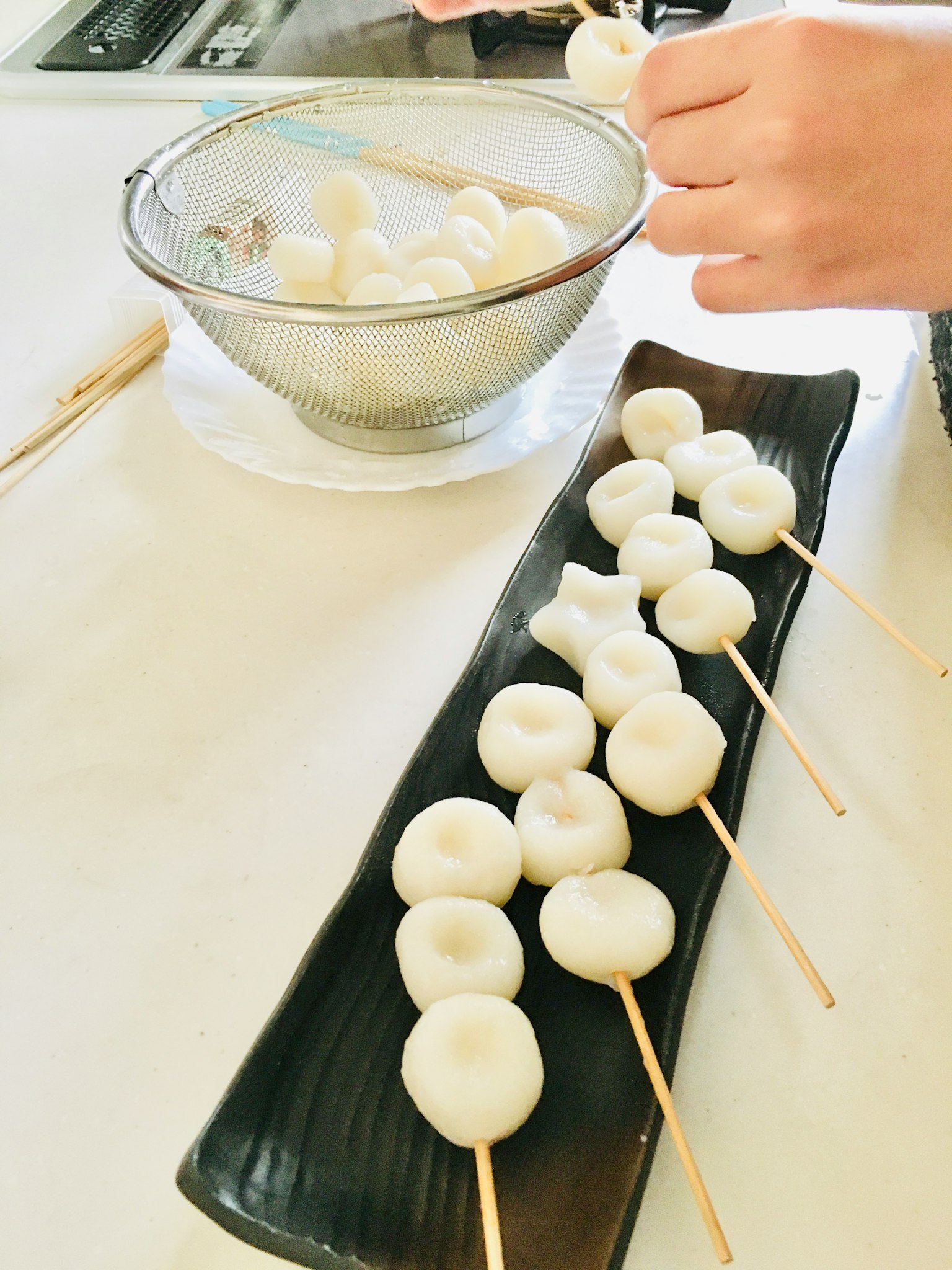 A hand preparing white dumplings on skewers with a bowl in the background
