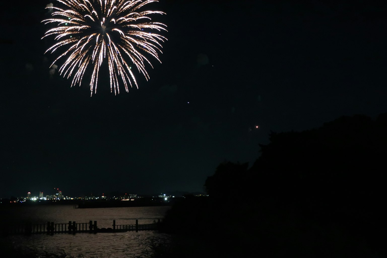 Fuegos artificiales estallando en el cielo nocturno sobre una superficie de agua brillante