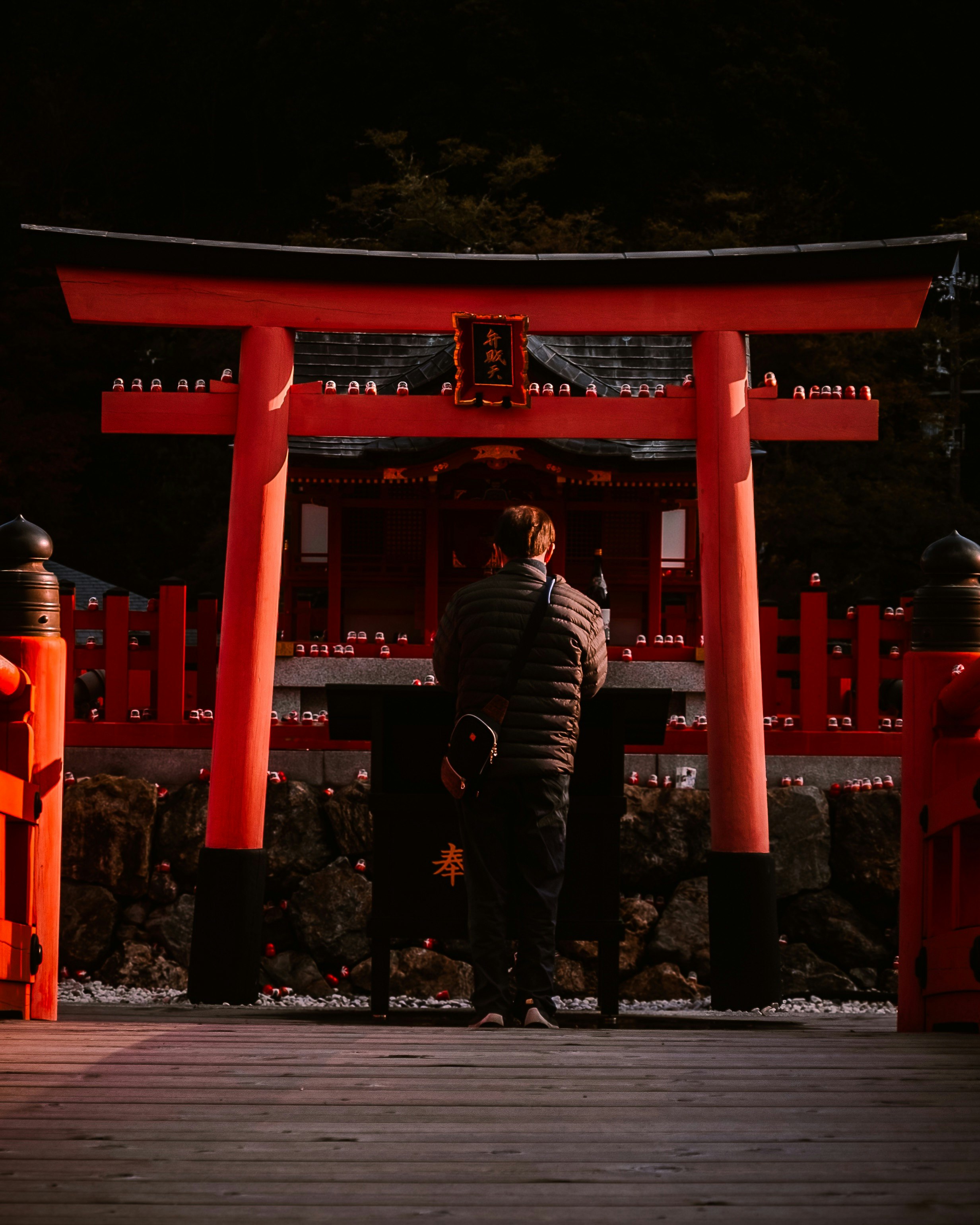 朱色の鳥居の前で立つ人物と提灯のある夜の神社の参道