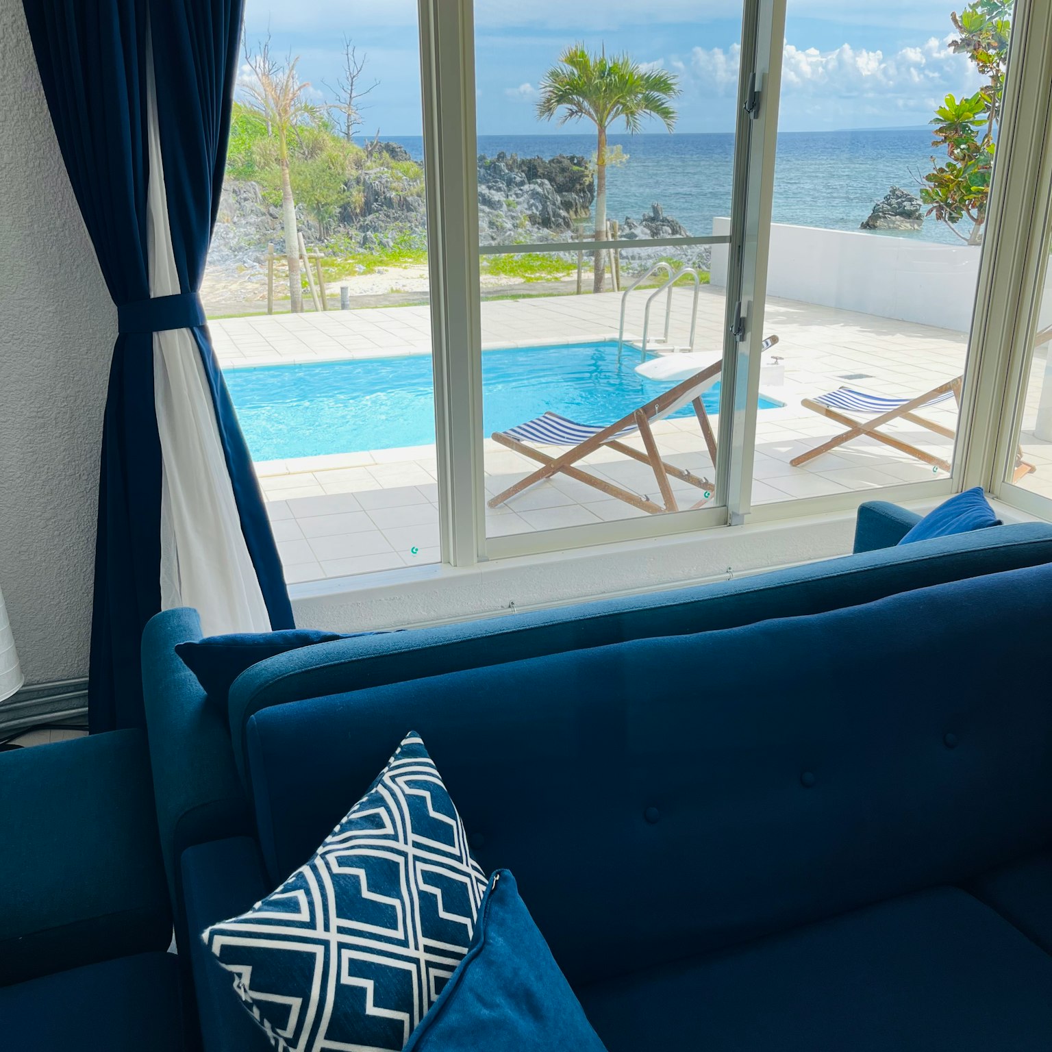 View of a pool and ocean from a blue sofa with decorative pillows
