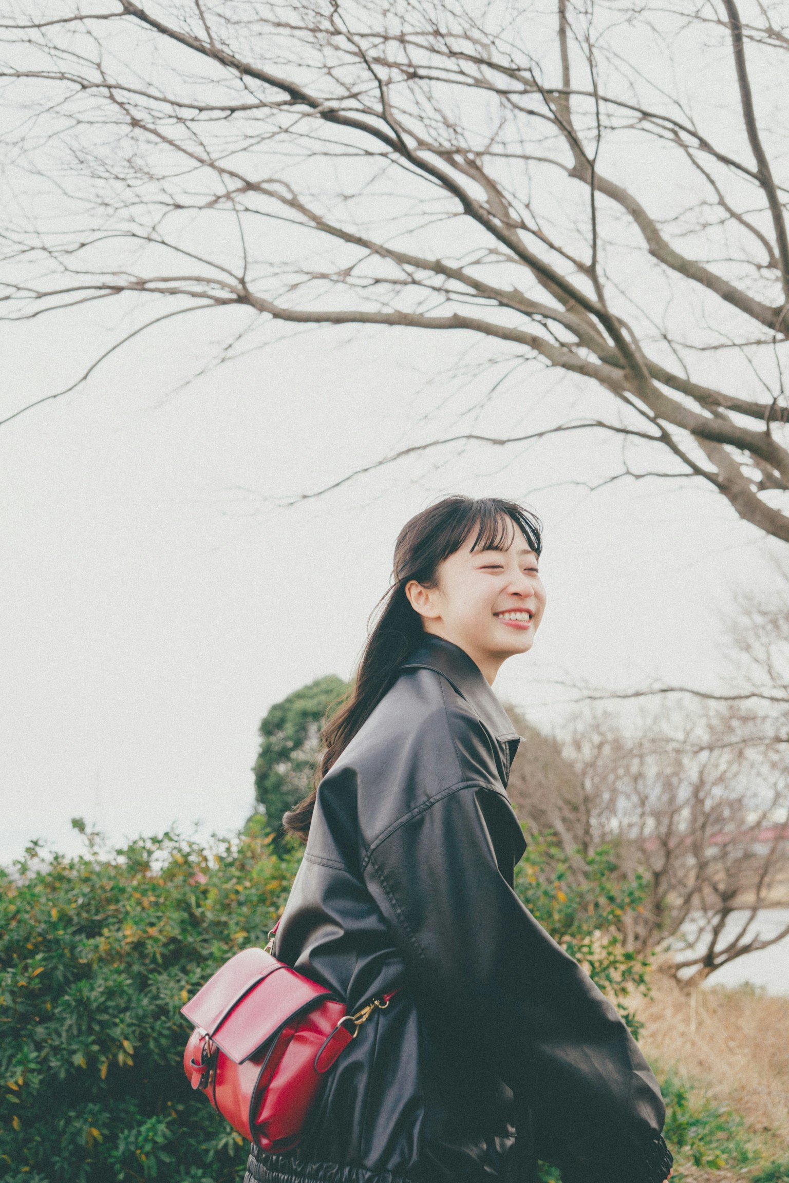 公园中微笑的女性穿着黑色外套并携带红色包包