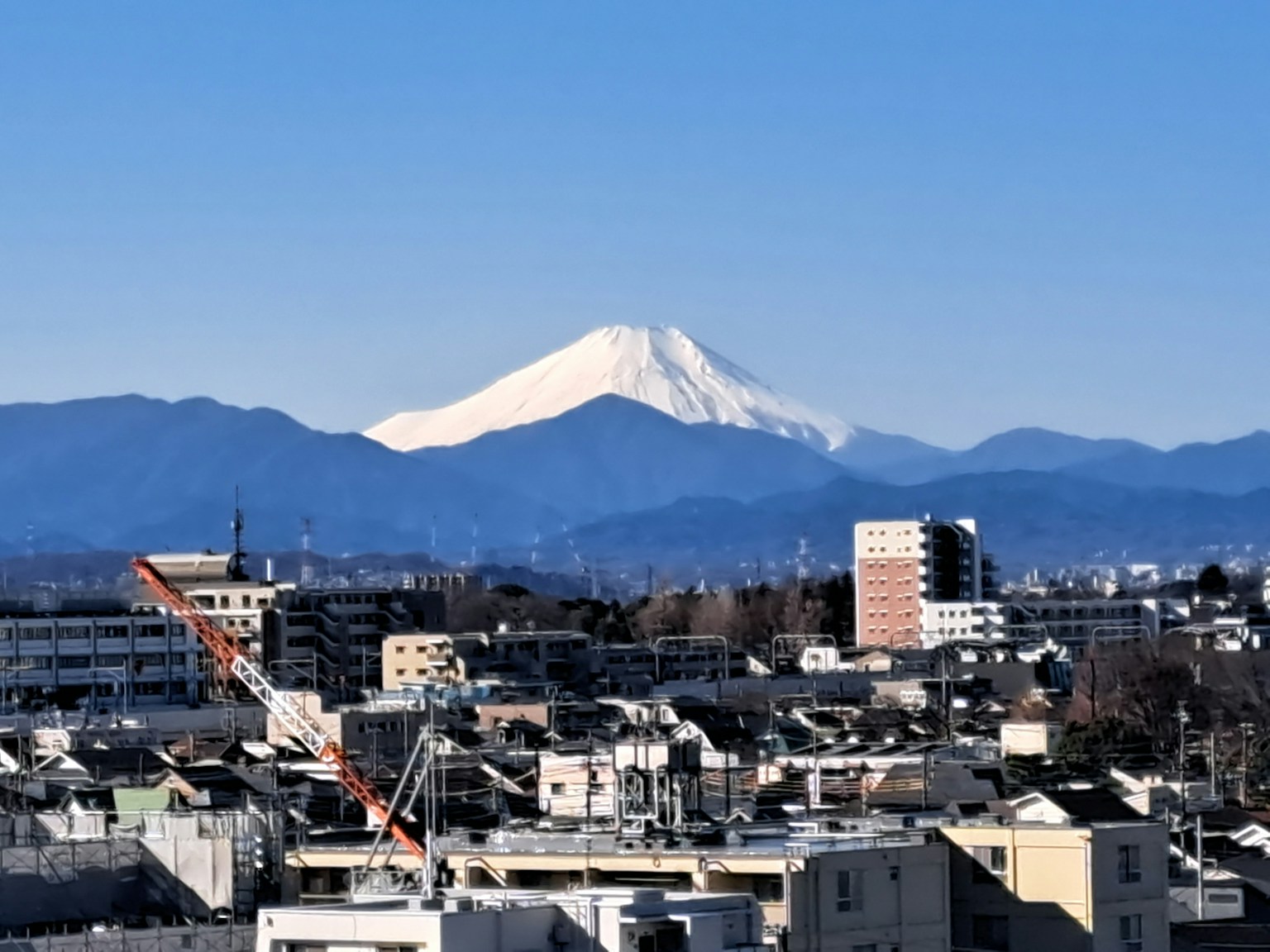 Paisaje urbano con el monte Fuji nevado bajo un cielo azul claro