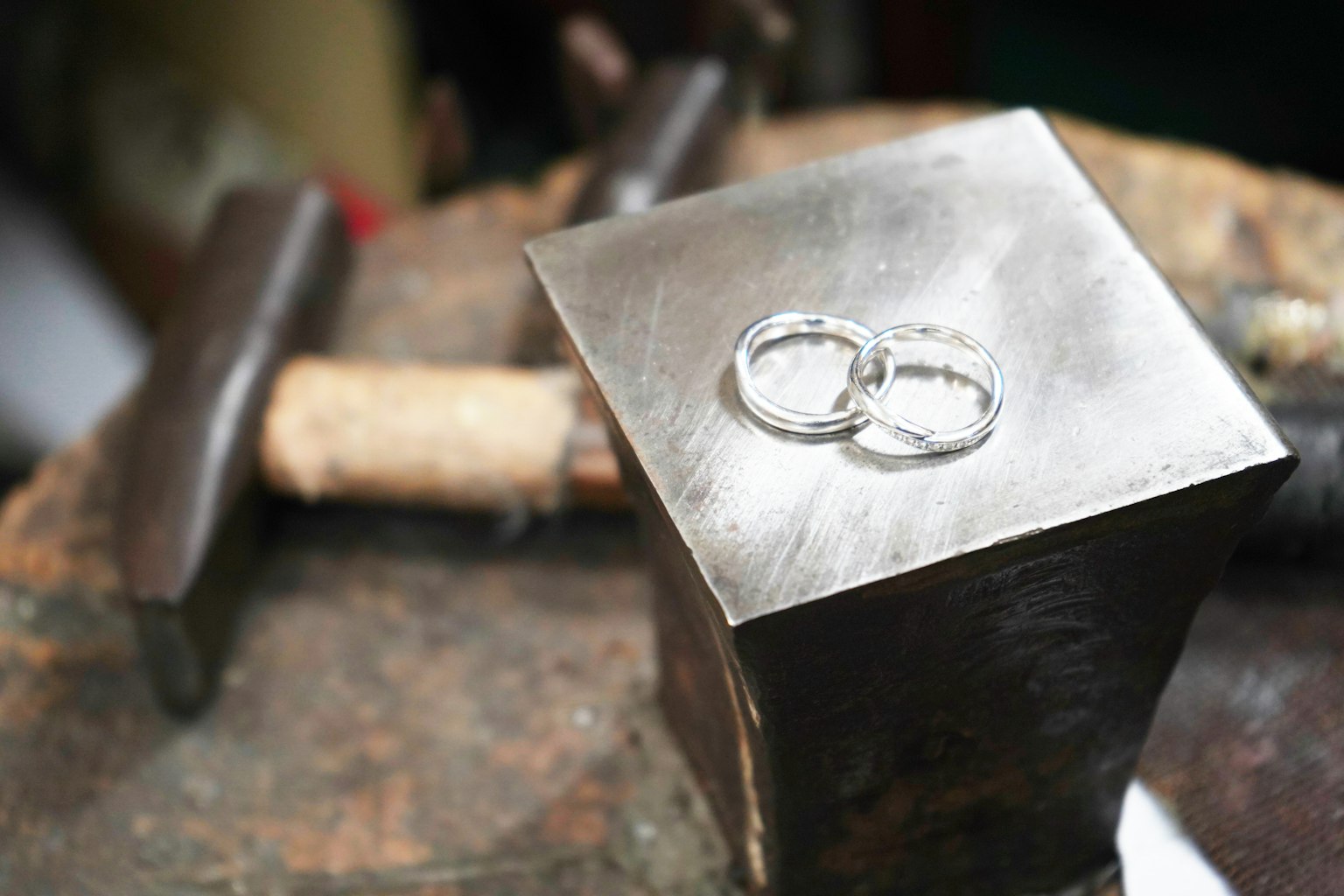Two silver rings placed on a metallic anvil with tools in the background