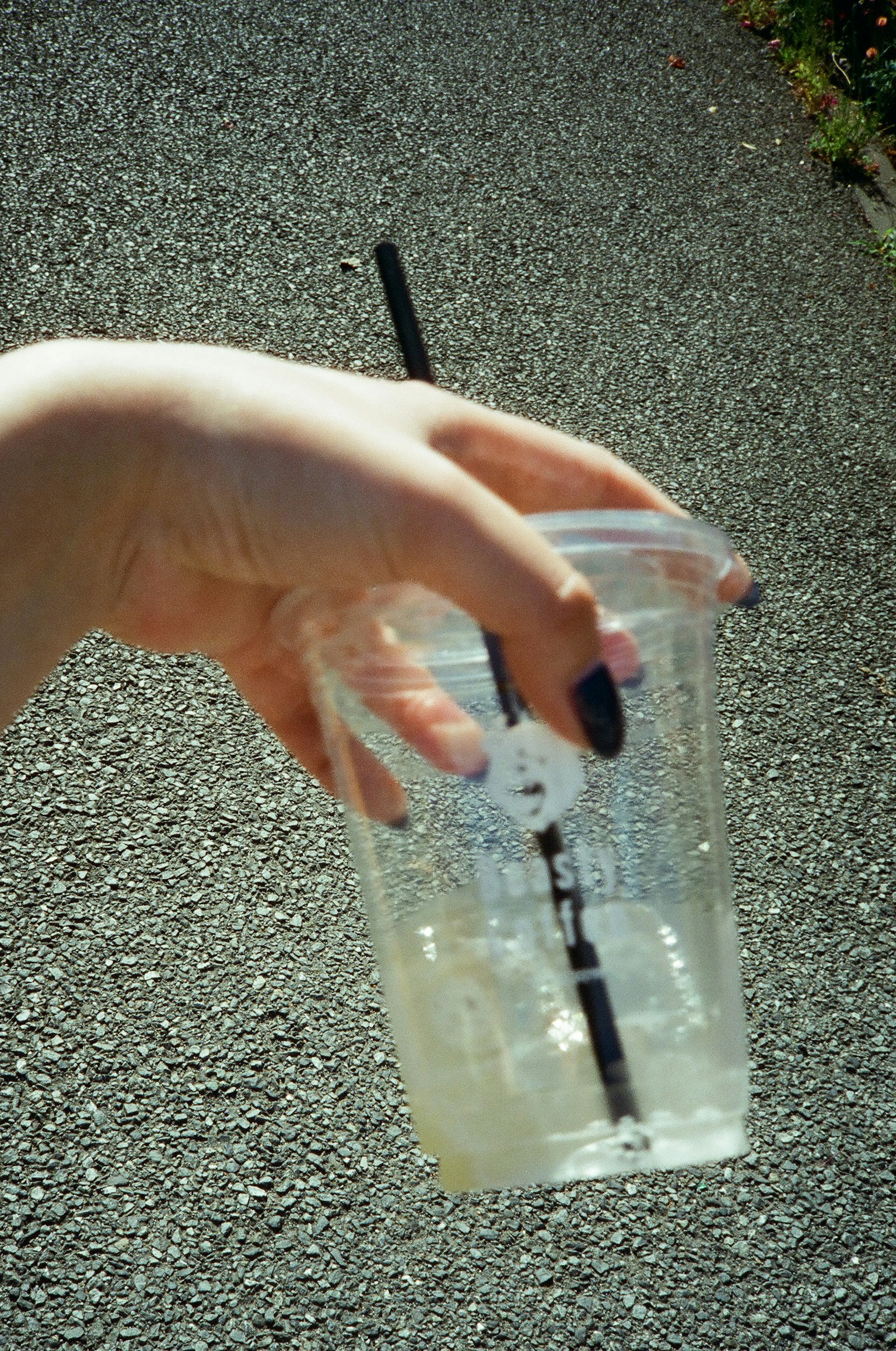 Hand, die einen transparenten Becher mit einem schwarzen Strohhalm und einem Eisgetränk vor einem Straßenhintergrund hält