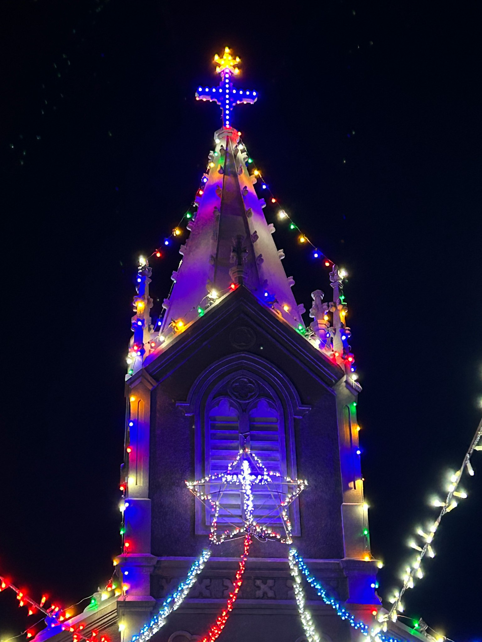 Clocher d'église orné de lumières de Noël colorées sous un ciel nocturne