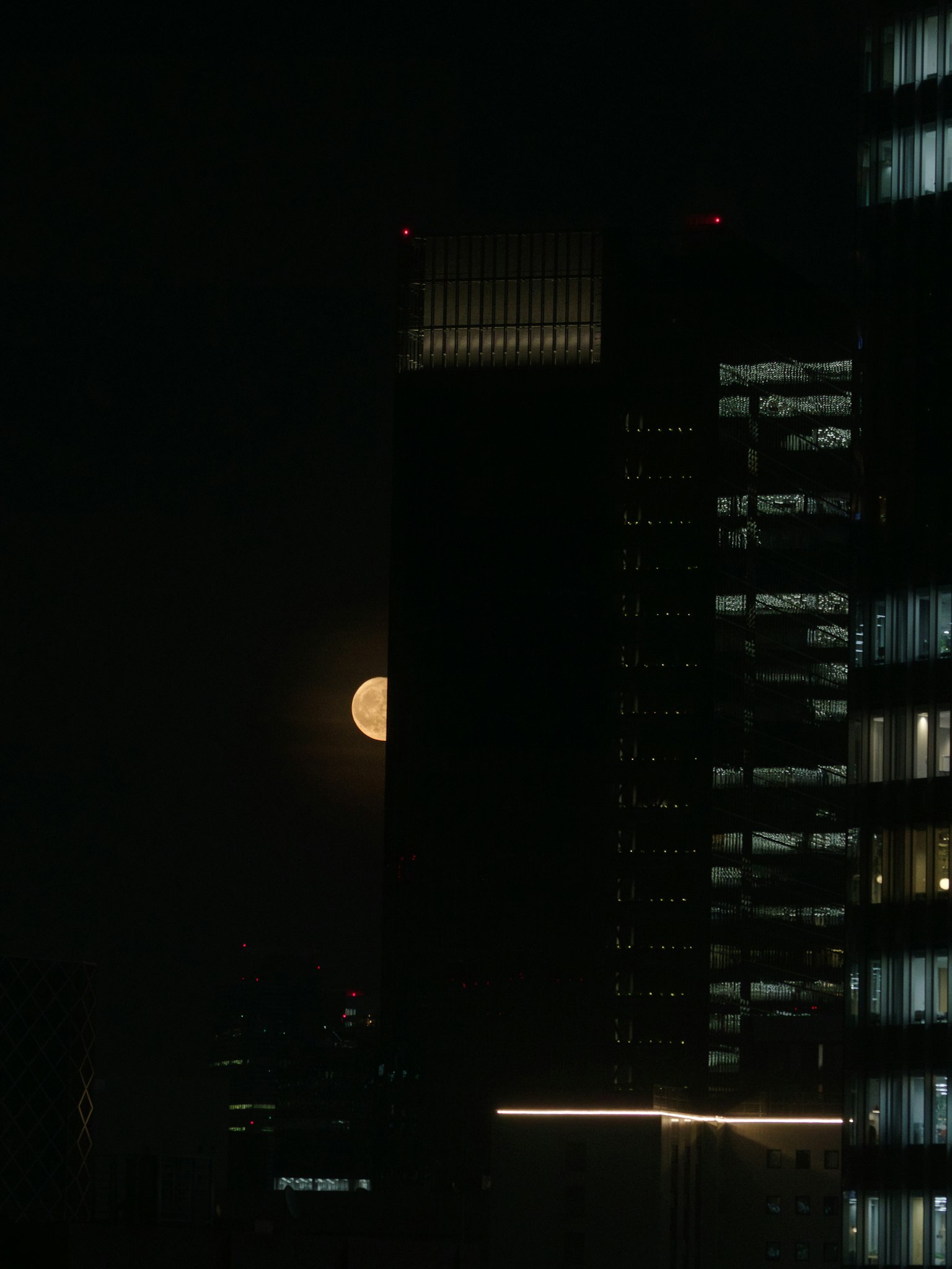 Großer Mond, der hinter Wolkenkratzern in einer nächtlichen Stadtlandschaft aufgeht