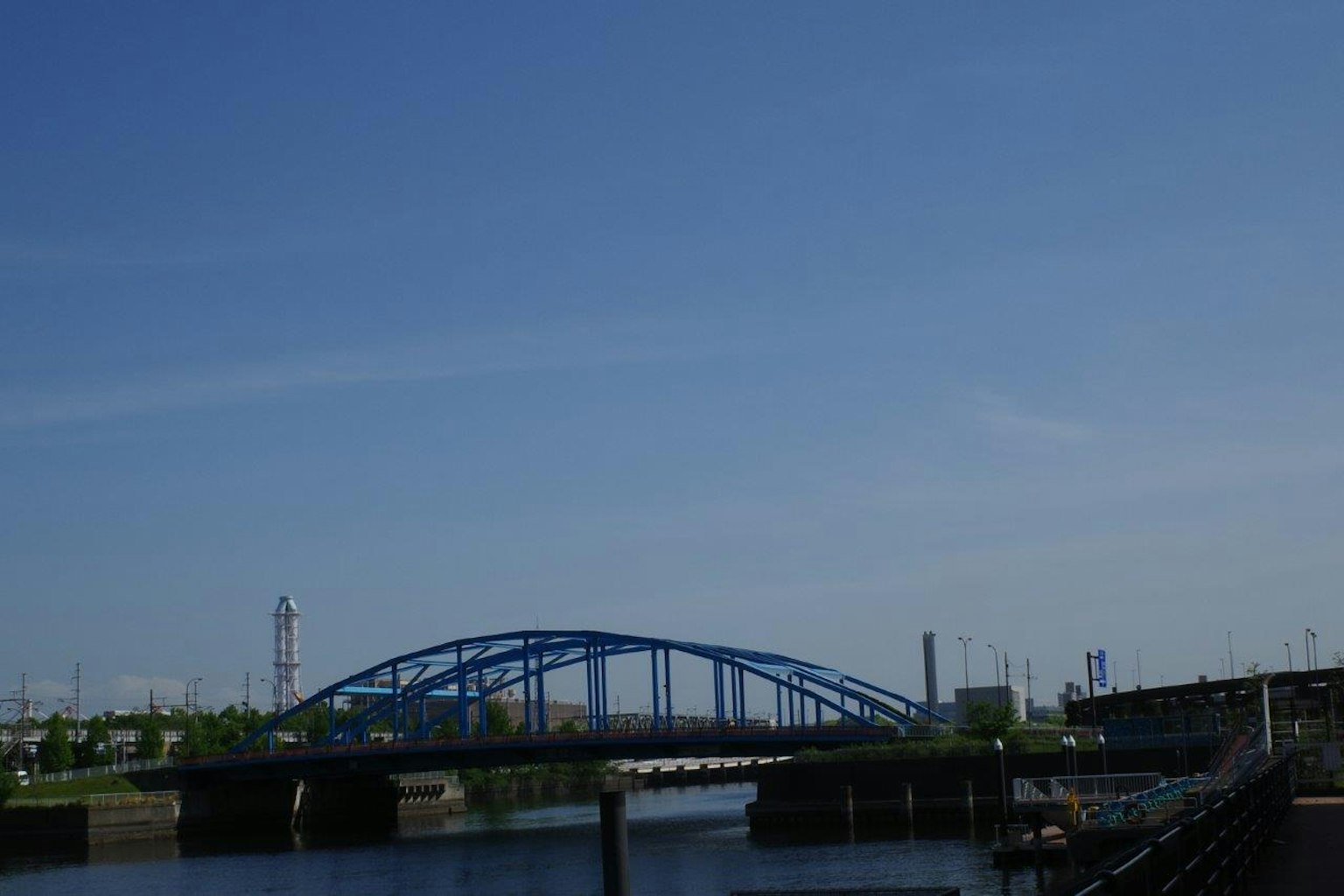 Un puente azul se extiende sobre un río tranquilo bajo un cielo claro