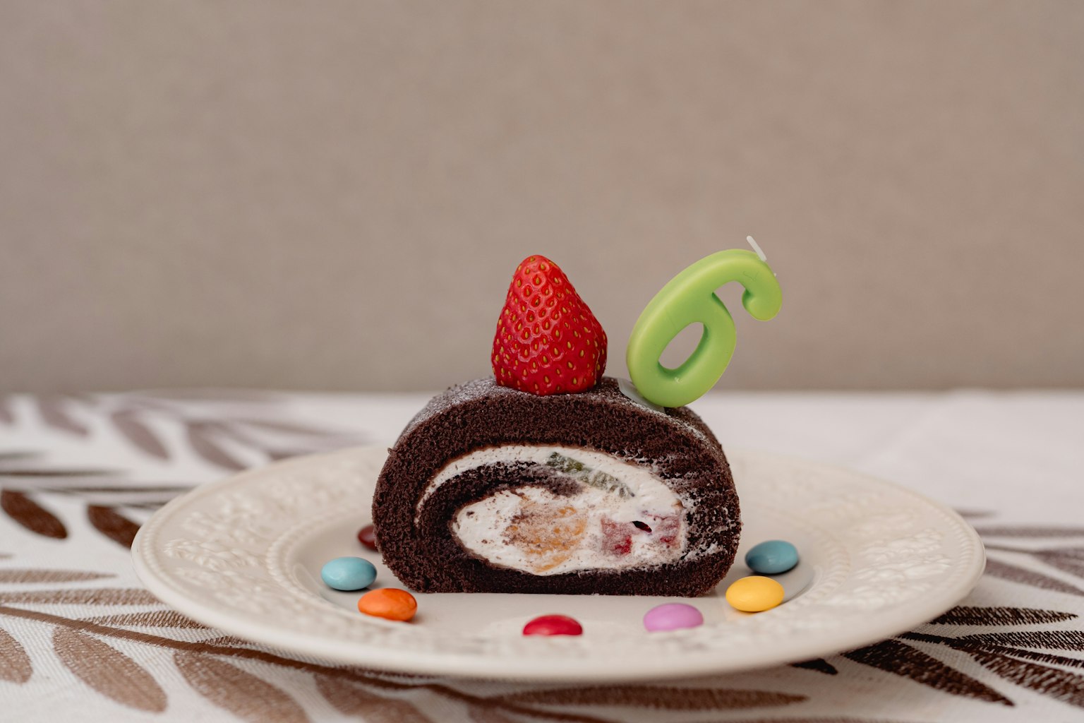 Irisan kue gulung cokelat dihiasi dengan stroberi dan lilin hijau