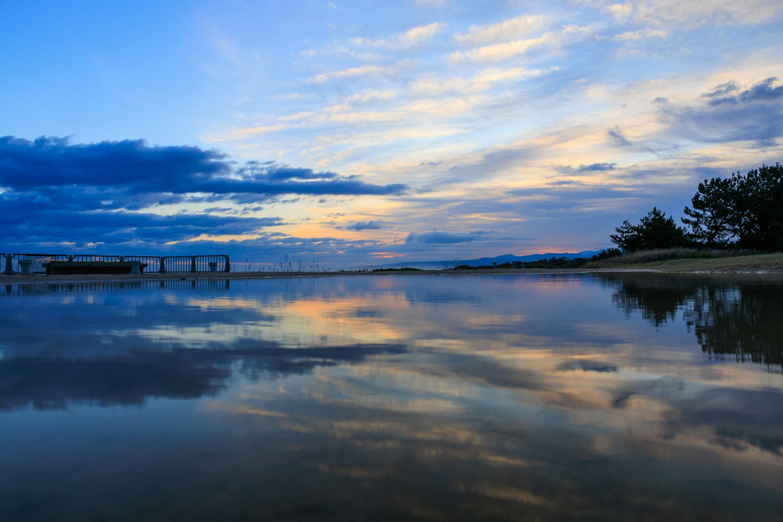 Pemandangan laut yang tenang dengan refleksi matahari terbenam yang cerah