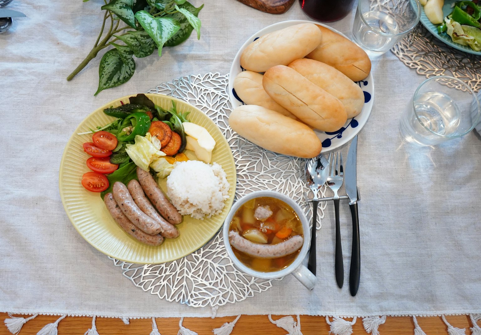 Une assiette de saucisses, légumes et riz avec un bol de soupe et une assiette de pain sur une table à manger