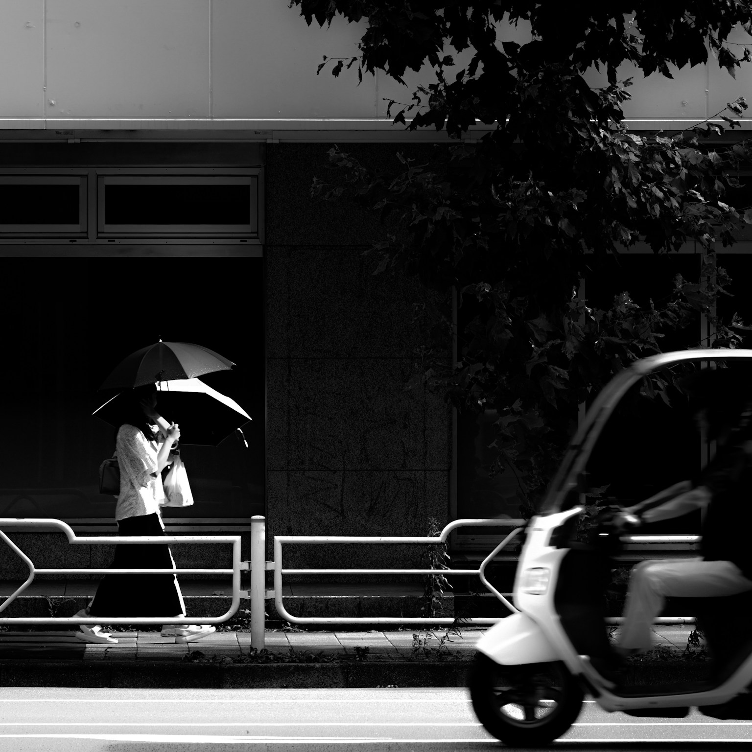 黑白照片，女人撐著雨傘走路，旁邊有一輛滑板車經過