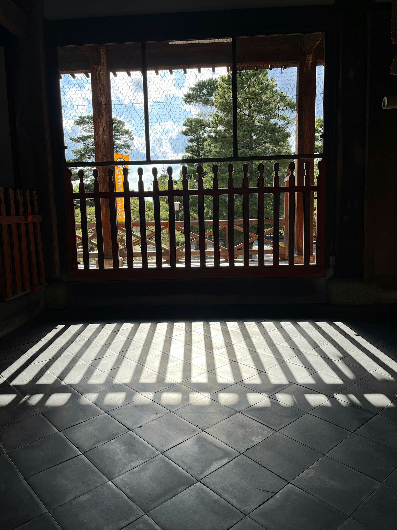 室內場景，窗戶透出光線在地板上投下陰影，外面有樹木