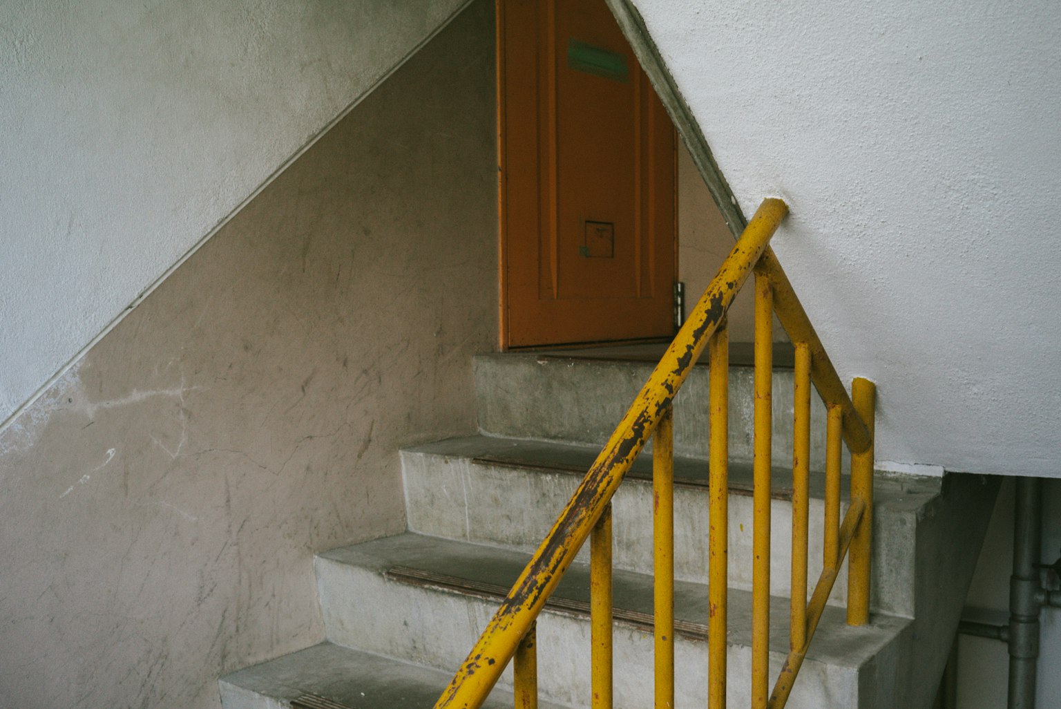 Concrete stairs with a yellow railing leading to an orange door