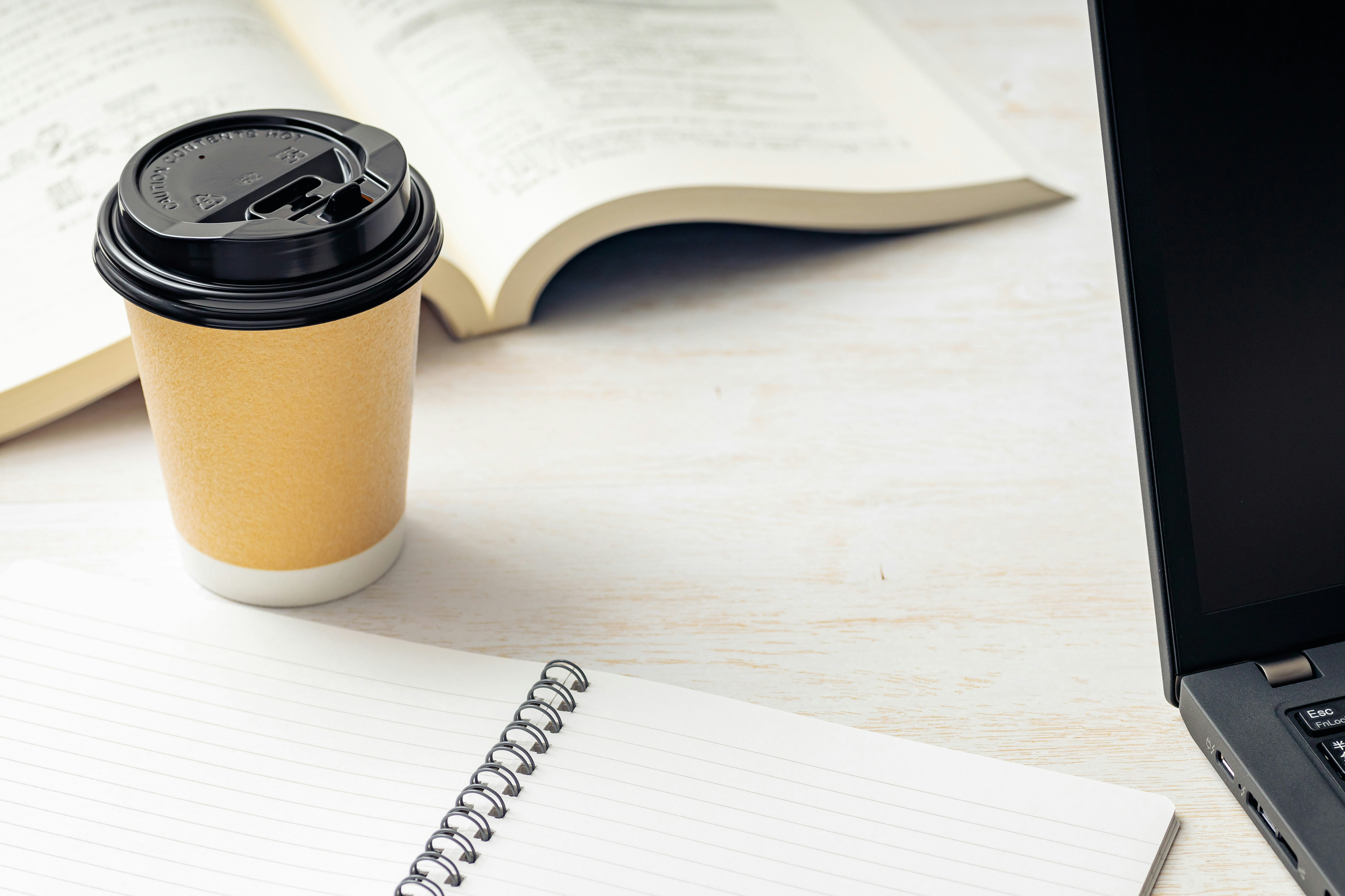 デスク上に置かれたコーヒーカップとノートパソコン 本とノートが周りに広がるシンプルな作業環境