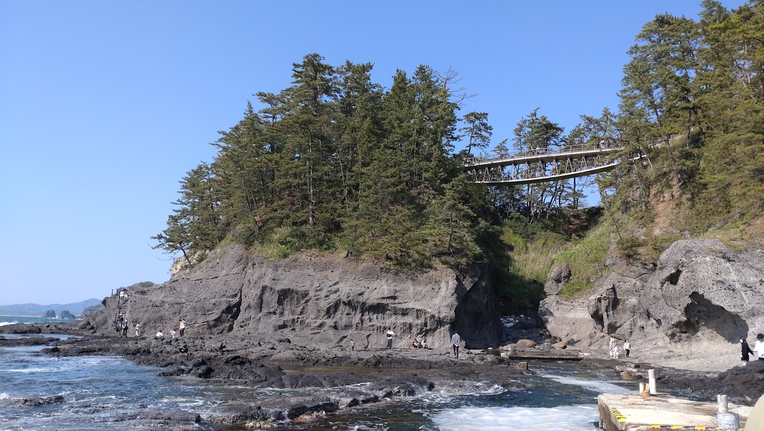 A bridge situated on a small hill surrounded by coastal rocks and trees