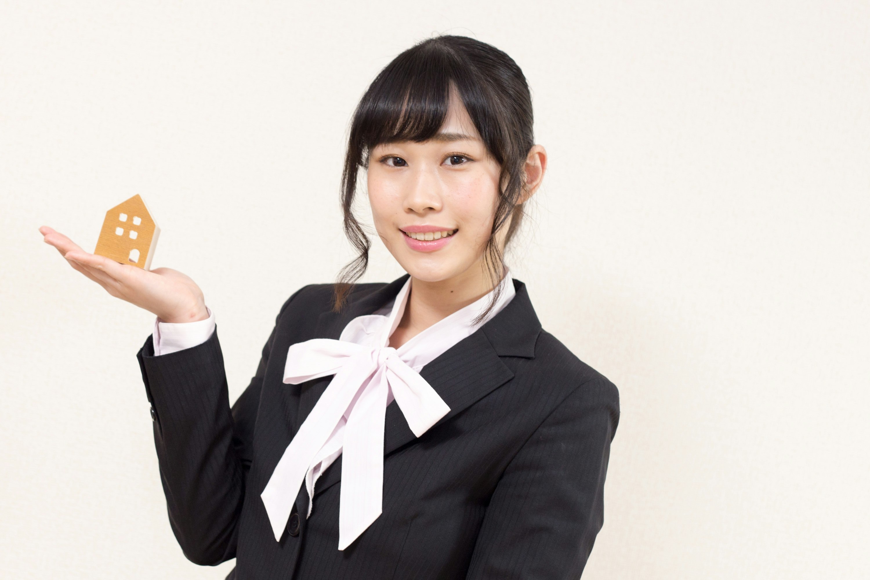 家の形の小物を持つスーツ姿の女性