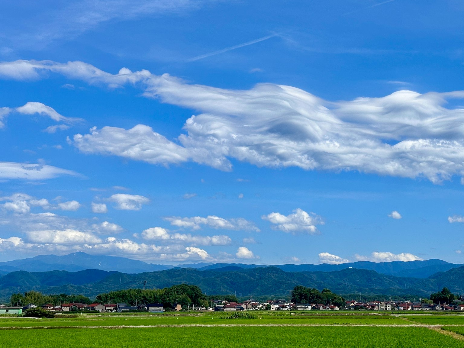 Saftige grüne Felder unter einem strahlend blauen Himmel mit fluffigen weißen Wolken und fernen Bergen
