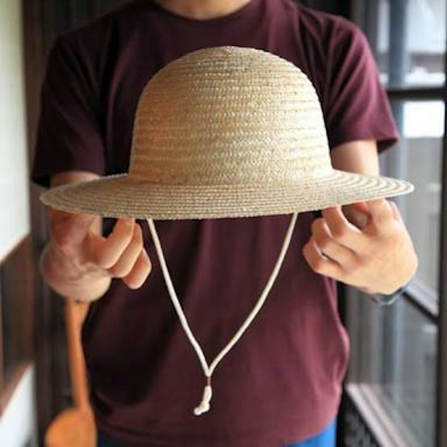 A person holding a straw hat with a chin strap