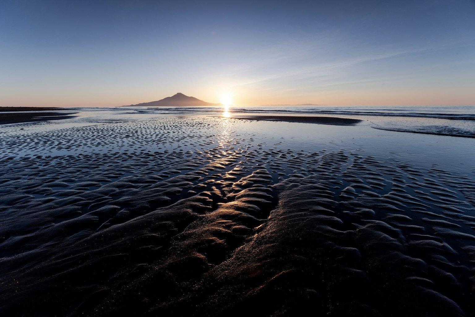 Sonnenuntergang über dem Ozean mit entfernten Bergen und nasser Sandtextur