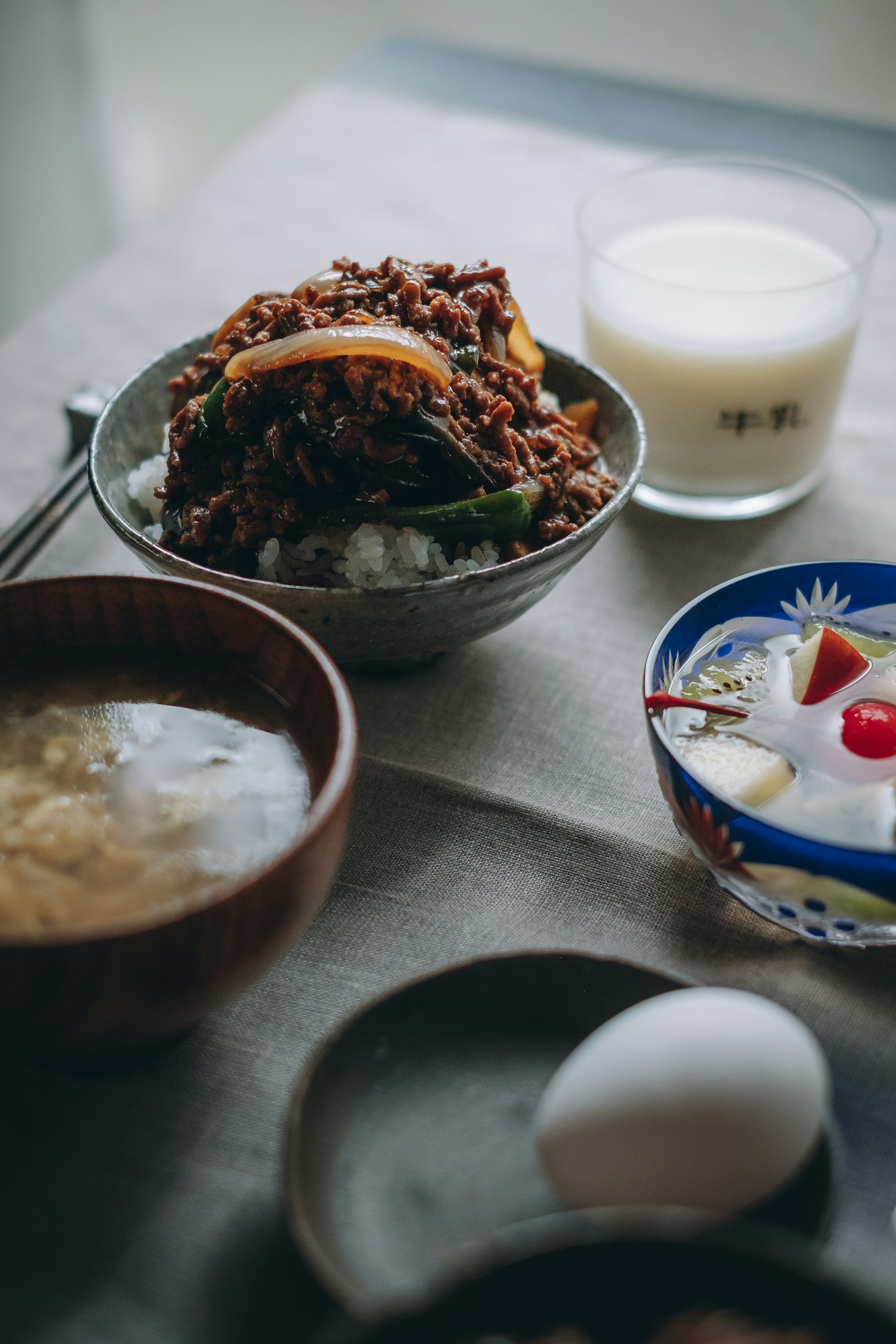 Comida japonesa con arroz cubierto de carne y verduras junto a leche y postre