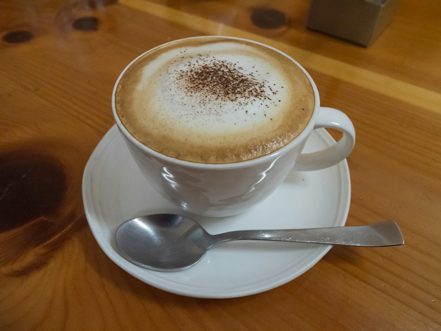 Latte krimi dalam cangkir putih dengan taburan bubuk kakao