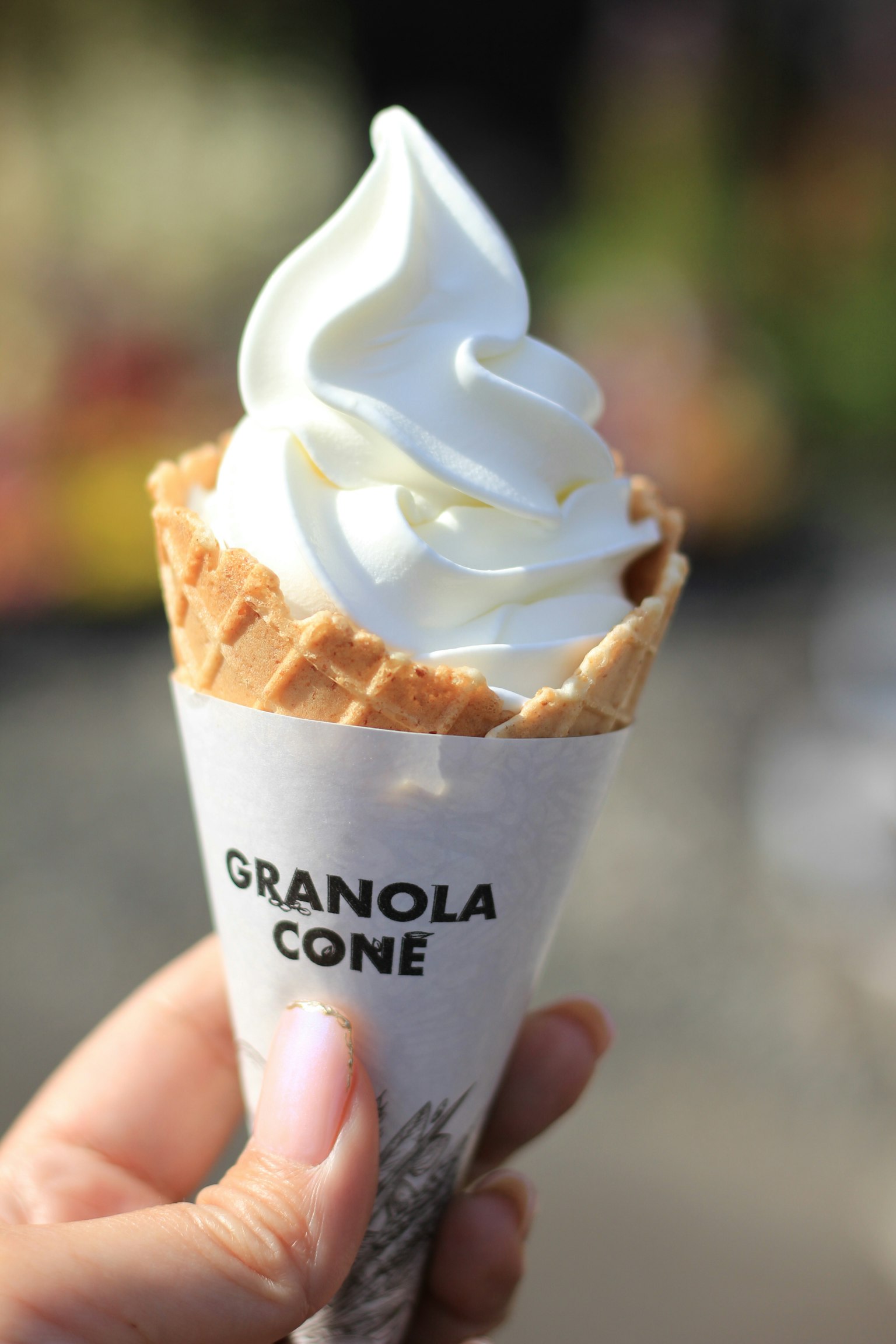 Es krim lembut dalam kerucut granola yang dipegang oleh tangan