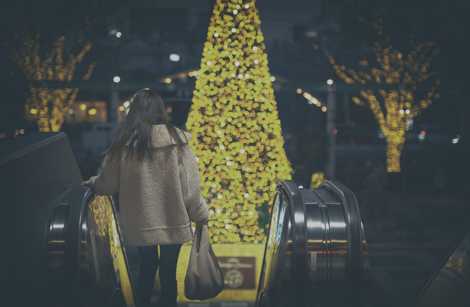 Donna che scende le scale mobili con un albero di Natale illuminato sullo sfondo