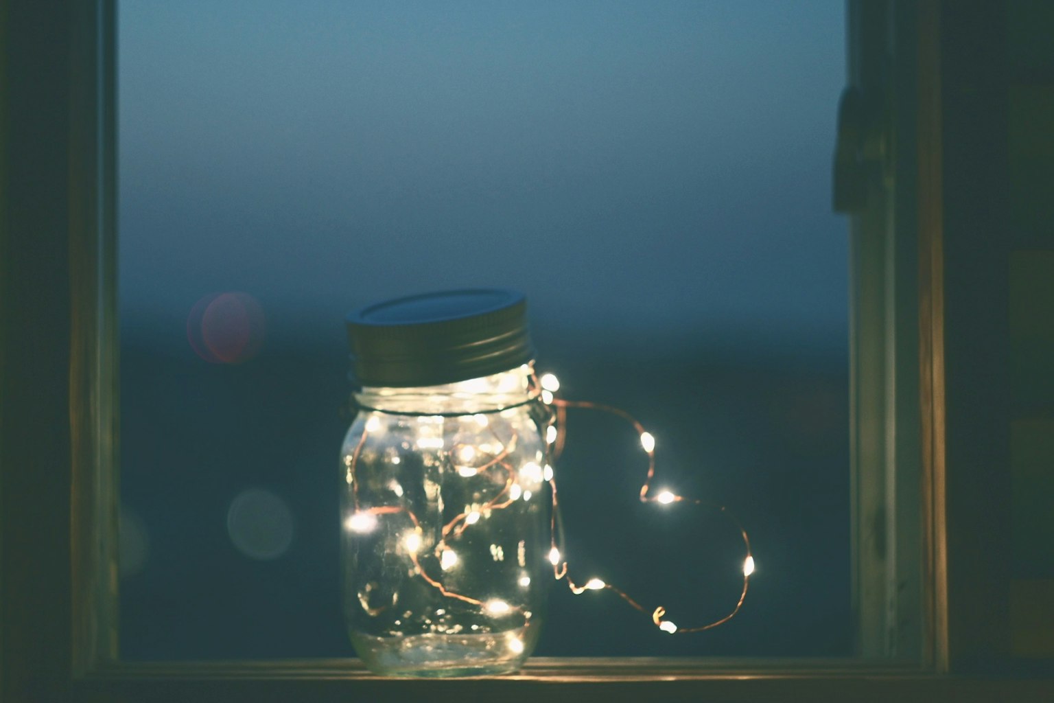窓辺に置かれた光る瓶とその周りに絡まったライト