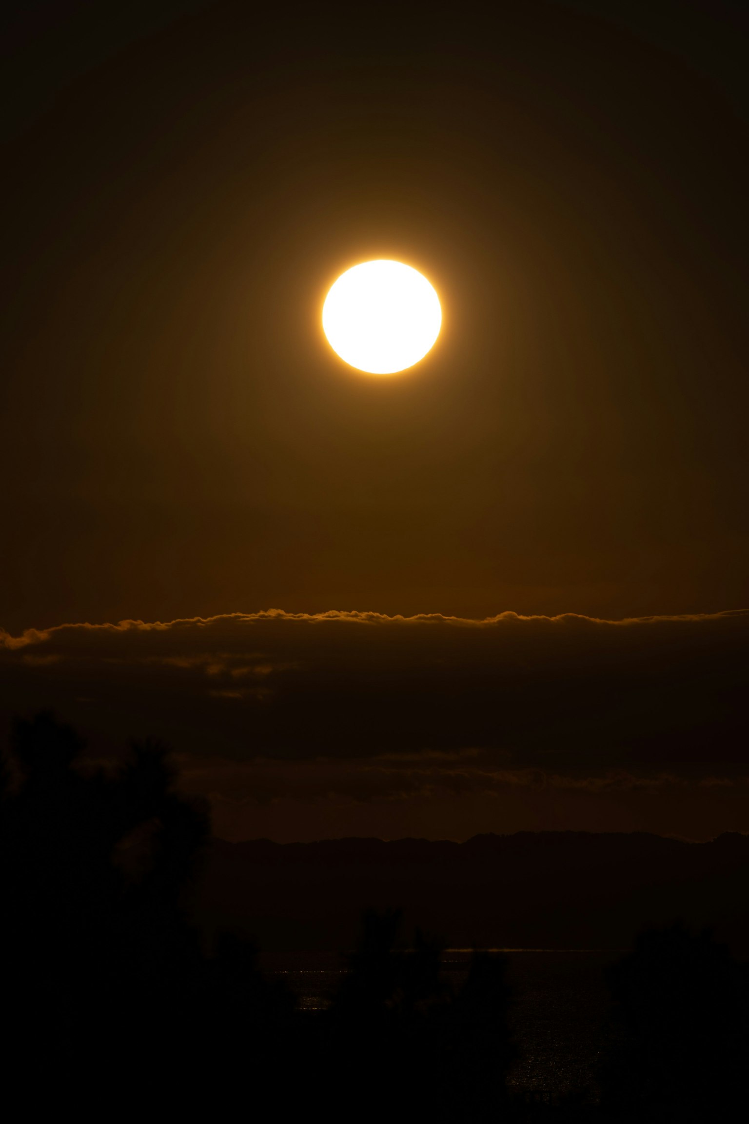 Large sun rising in a twilight sky with silhouetted clouds