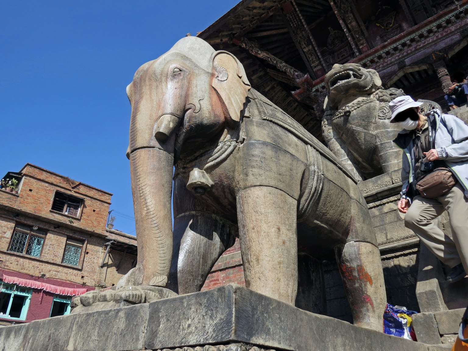 Patung gajah dari batu dengan arsitektur tradisional di latar belakang