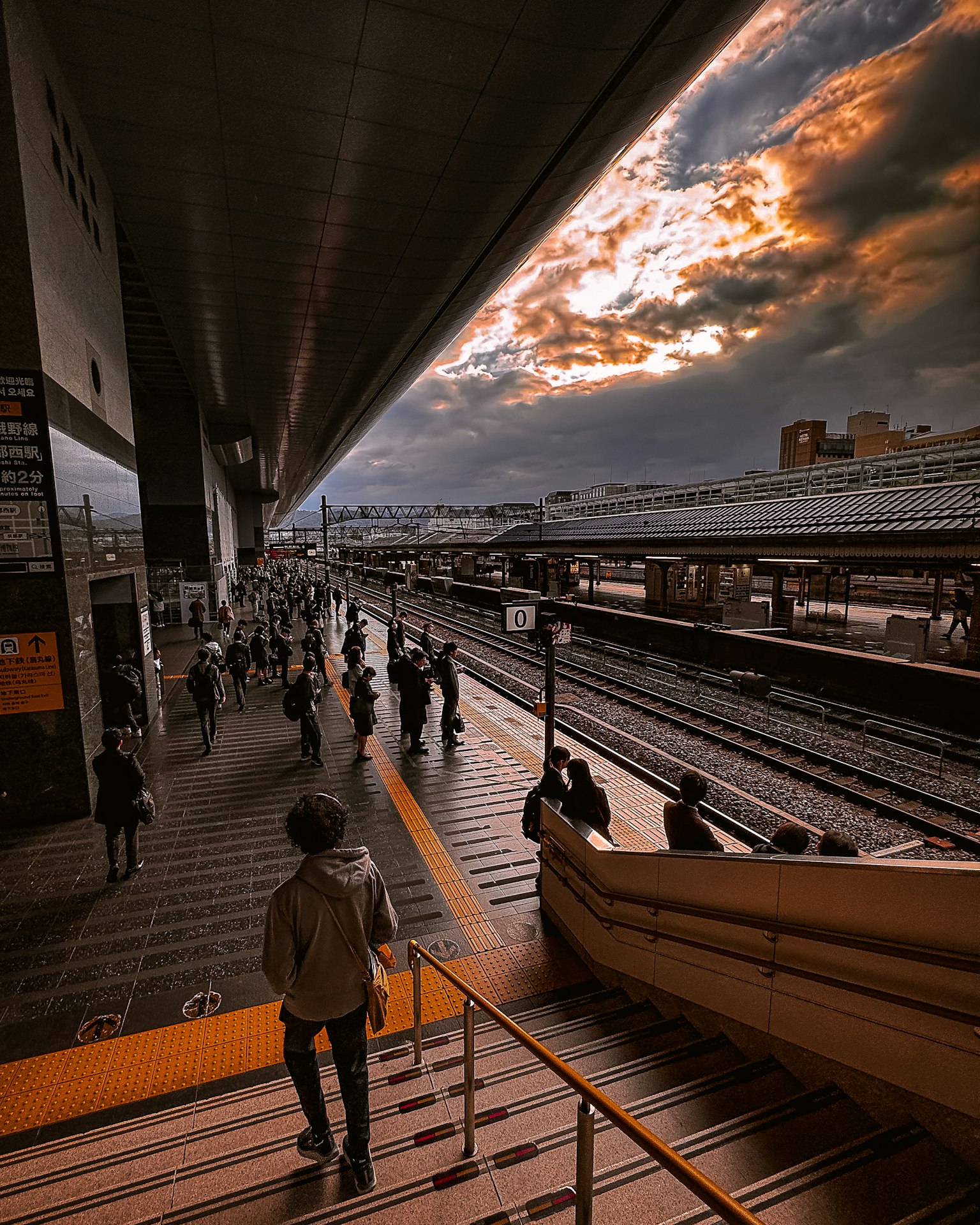 Folla di persone su una piattaforma ferroviaria con un cielo al tramonto drammatico