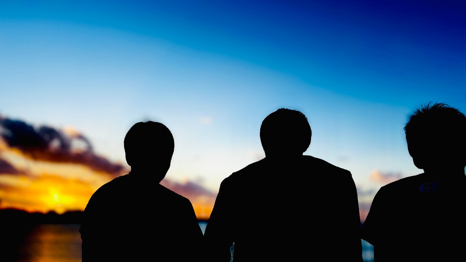 夕日を背にした三人のシルエットが美しい空を見つめる
