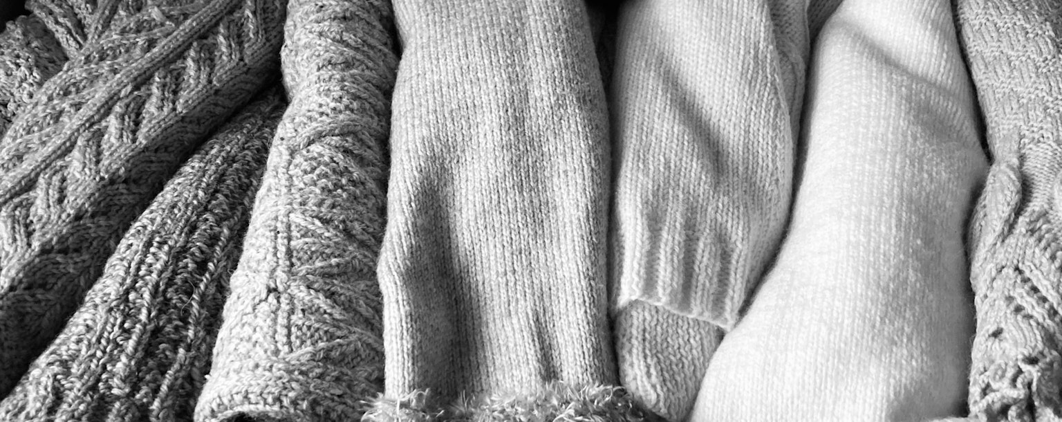 Ein Schwarzweißfoto von verschiedenen strukturierten Strickpullovern, die zusammen angeordnet sind