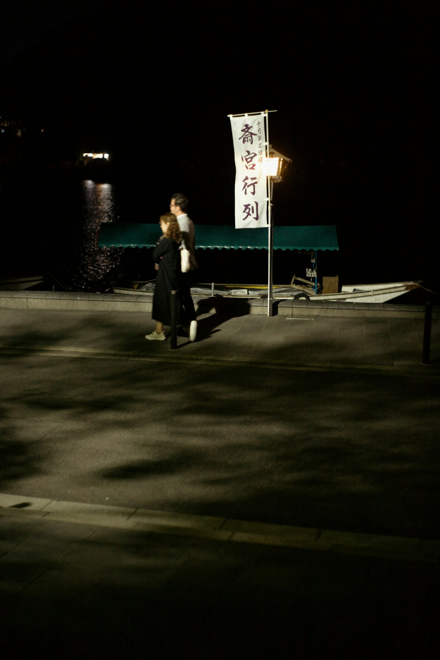 People walking at night by the harbor with a lantern sign