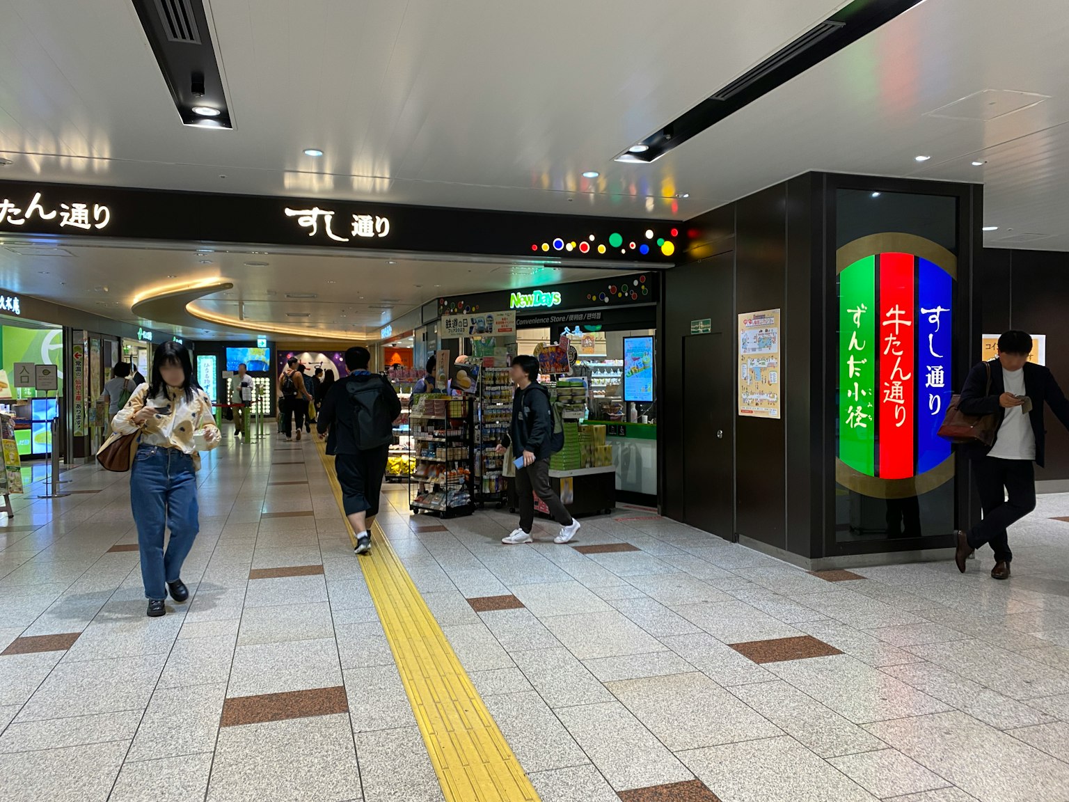 Vue intérieure d'une gare animée avec des personnes marchant des panneaux colorés et un éclairage lumineux