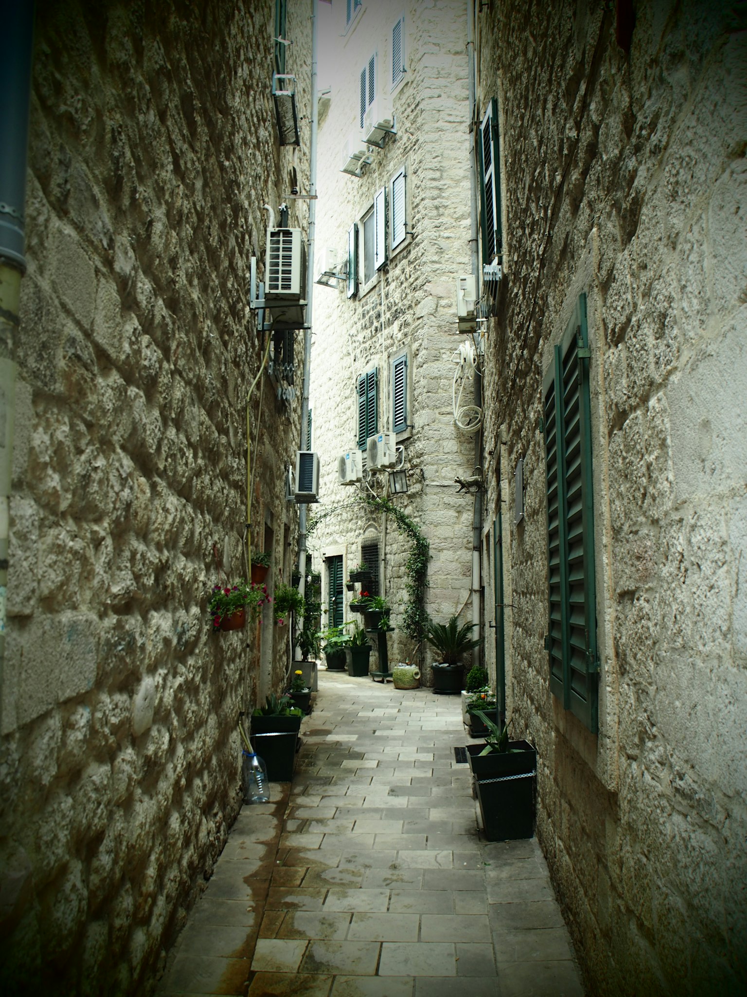 Narrow alleyway with stone walls and potted plants in a historic setting