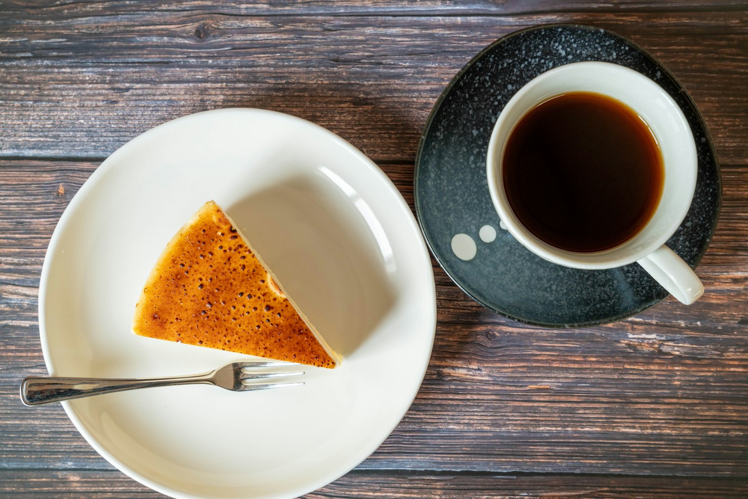 Una porción de pastel en un plato blanco junto a una taza de café