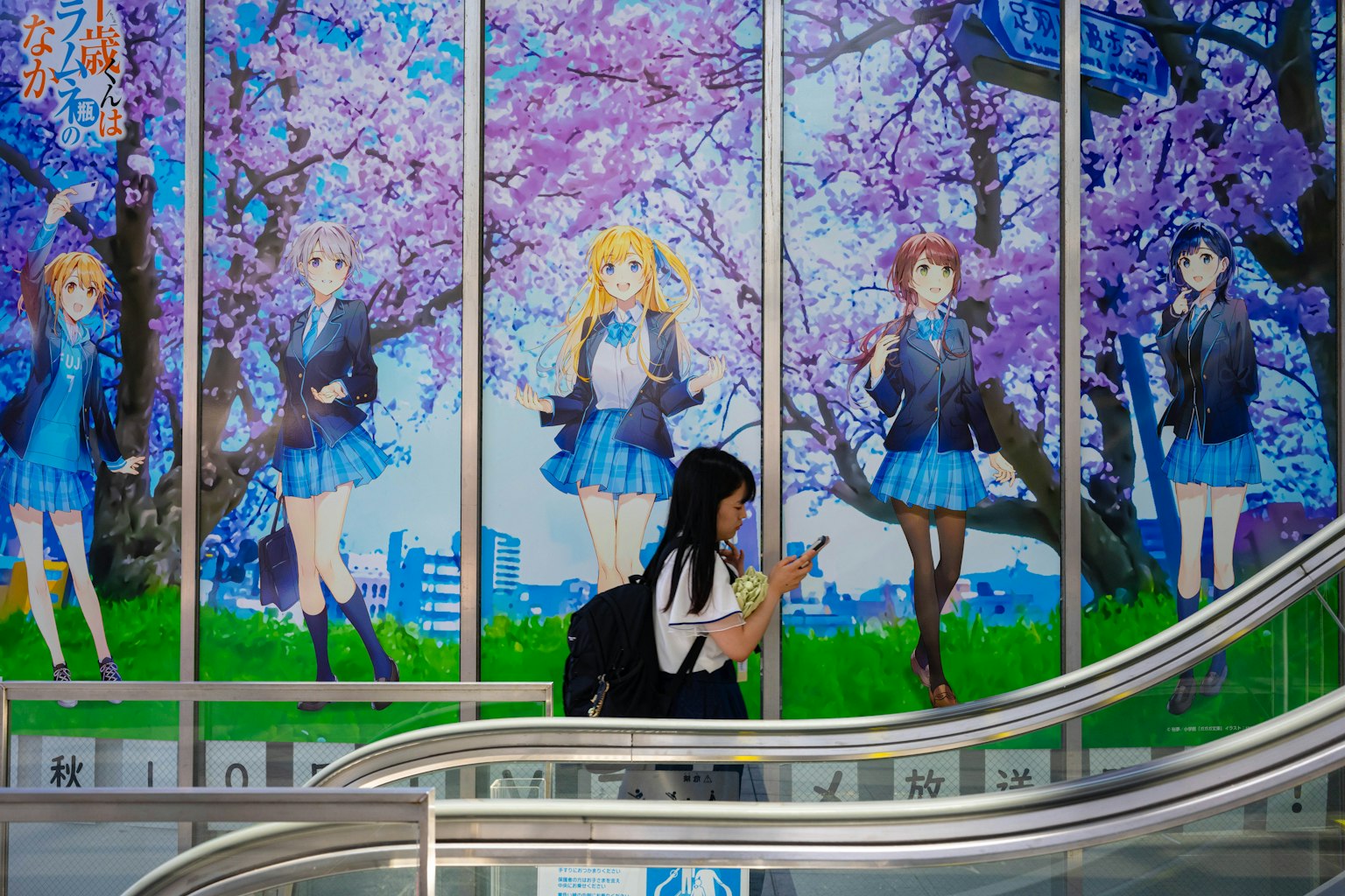 Una donna con uno smartphone davanti a un muro con personaggi di anime tra ciliegi in fiore