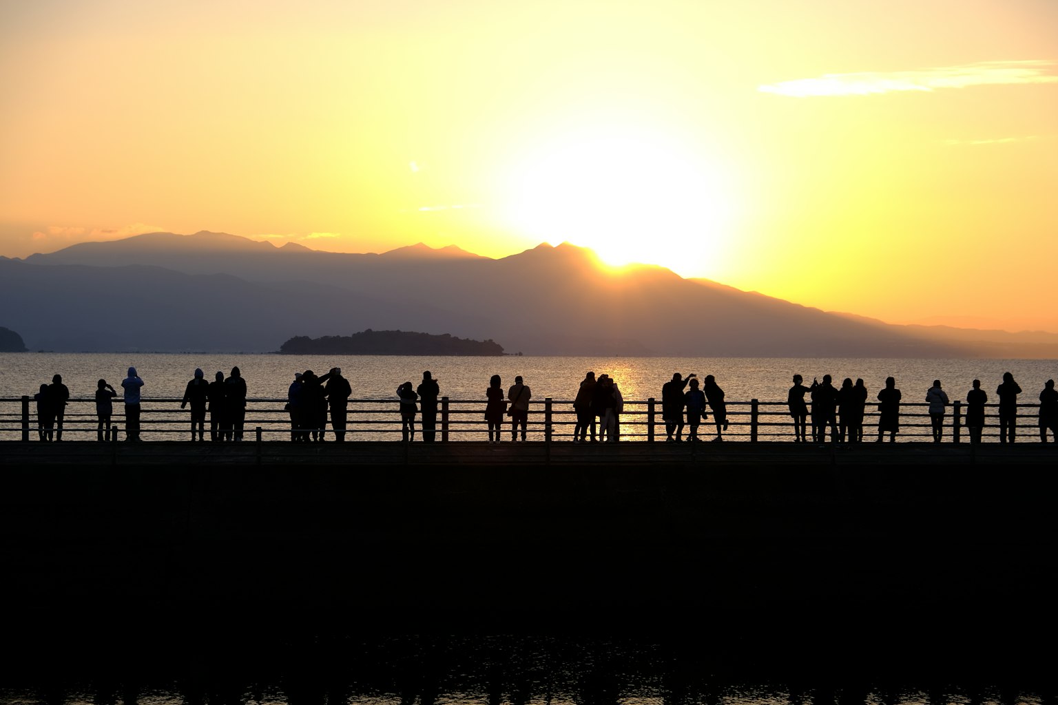 เงาของผู้คนที่ยืนอยู่ท่ามกลางพระอาทิตย์ตกดินและภูเขาในพื้นหลัง