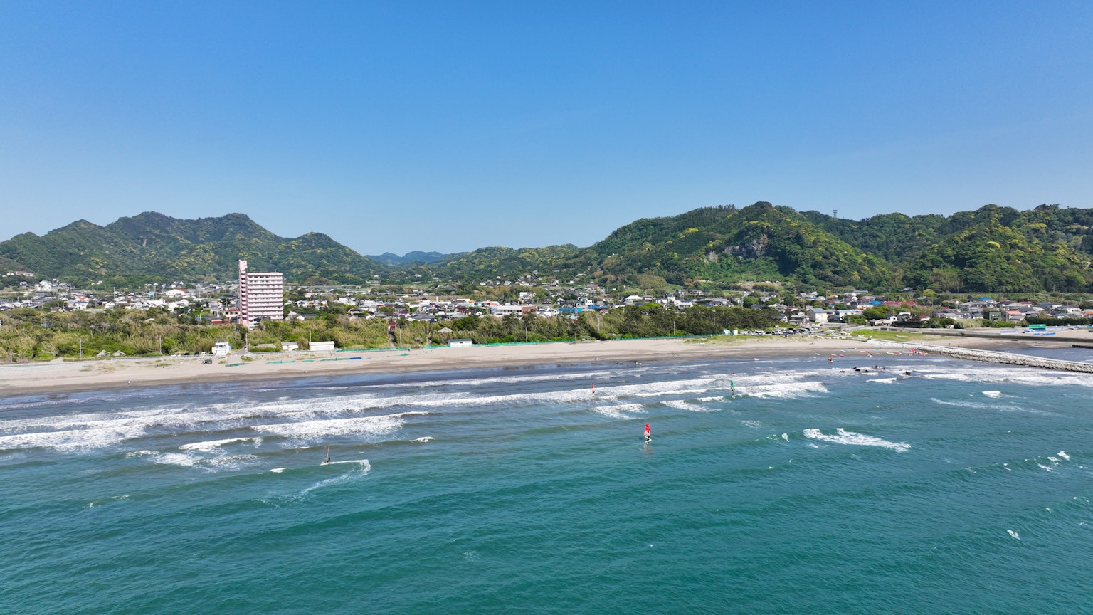 美麗的海灘景觀，藍色海洋和白色浪潮 背景中有綠色山脈和寧靜的小鎮