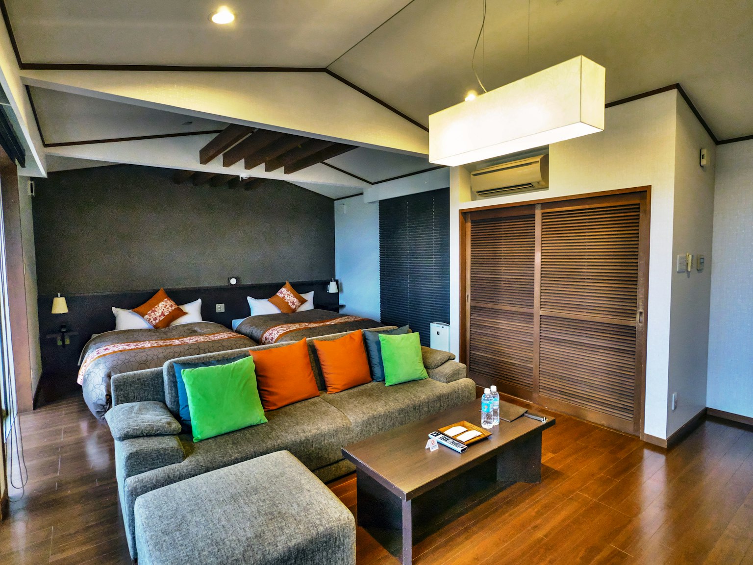 Habitación moderna con dos camas, un sofá con cojines coloridos y suelo de madera