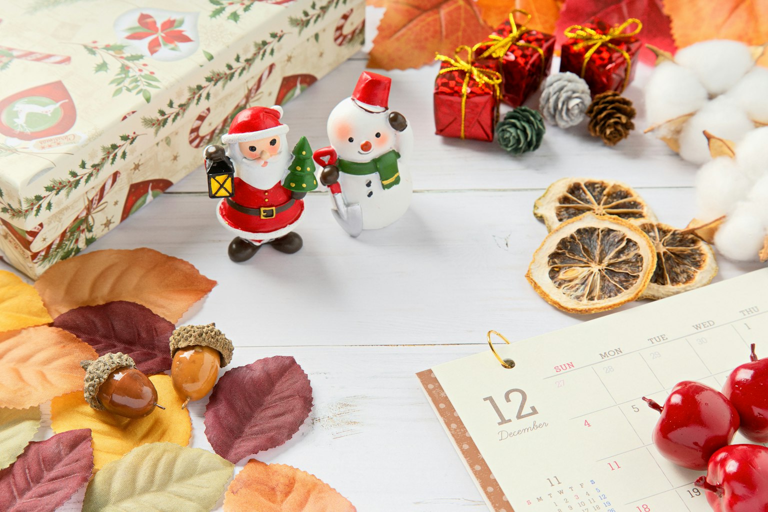 Pengaturan meja dengan patung Santa dan manusia salju dikelilingi oleh hadiah Natal dan daun musim gugur