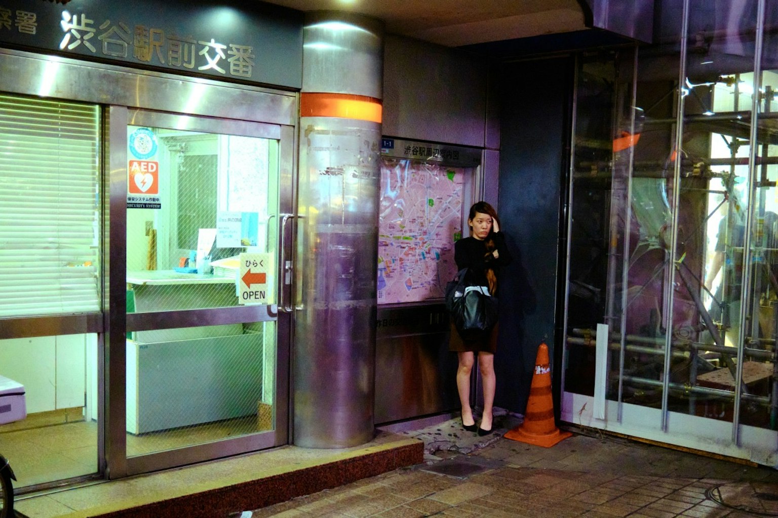 Woman standing by a map near Shibuya Crossing at night with bright signage