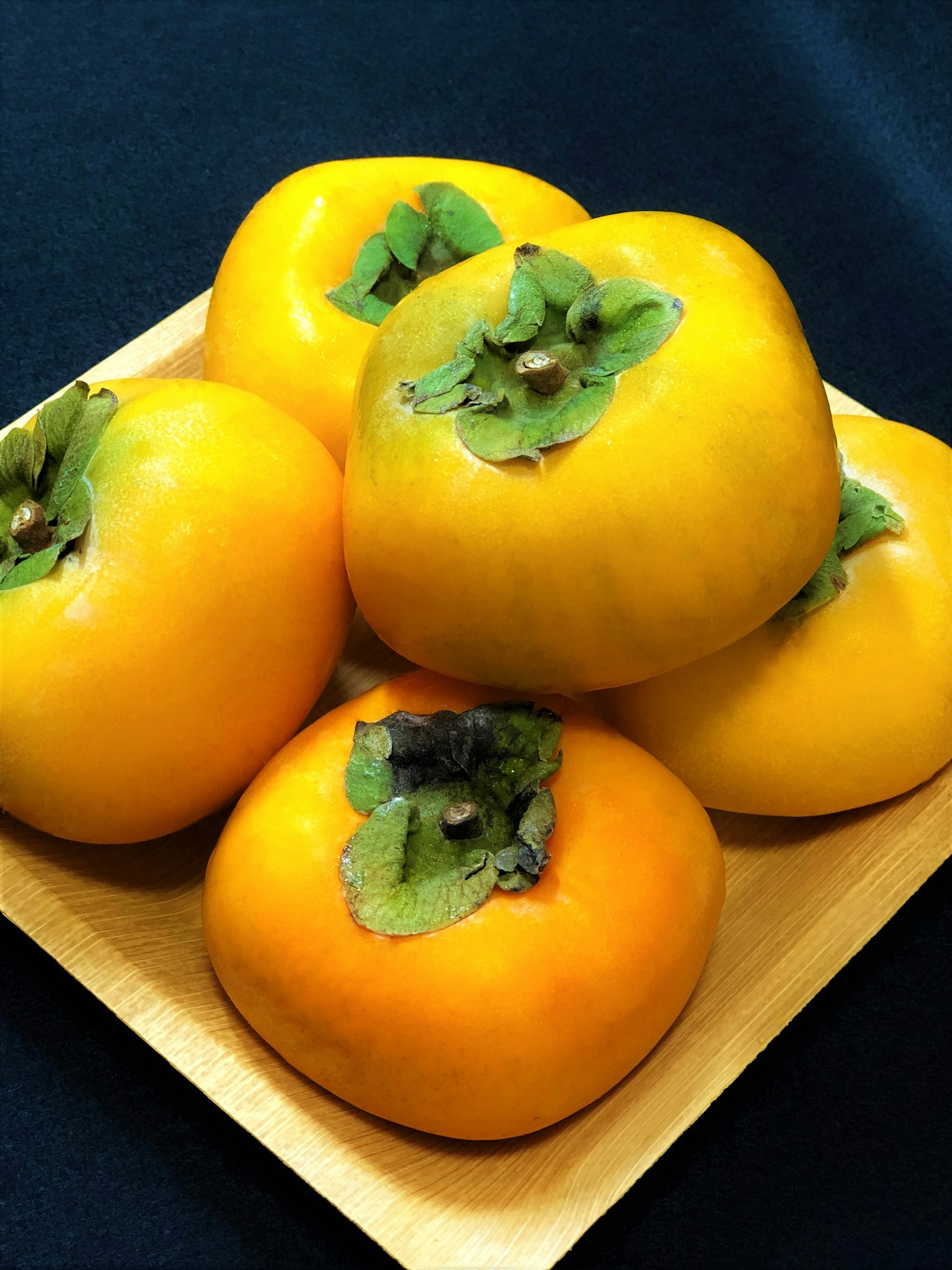Persimonas naranjas vibrantes dispuestas en un plato de madera