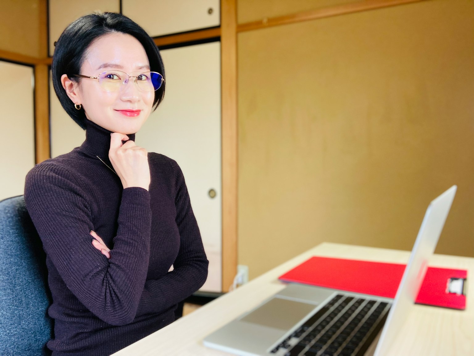 책상에 앉아 검은색 터틀넥을 입고 안경을 쓴 여성이 사색에 잠긴 모습