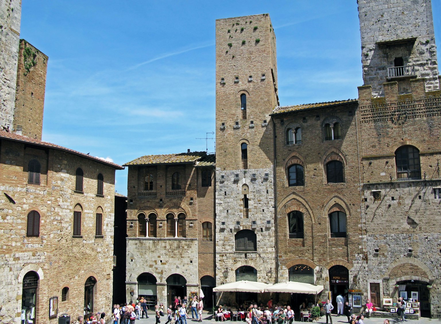 Orang-orang berkumpul di alun-alun San Gimignano dikelilingi oleh arsitektur abad pertengahan